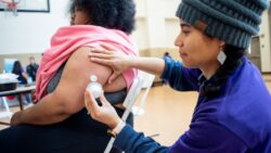 Photo of health worker attending to a patient's arm implant in a school gymnasium.