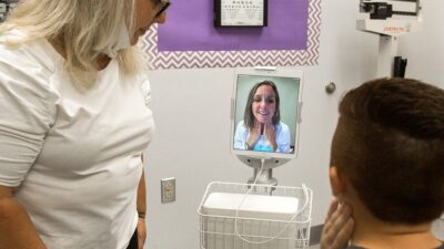 Young patient having an e-visit with doctor while nurse observes.