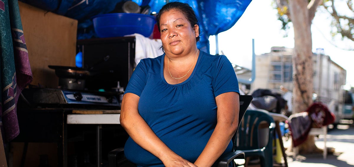 Woman experiencing homelessness sits under a tarp with her belongings.