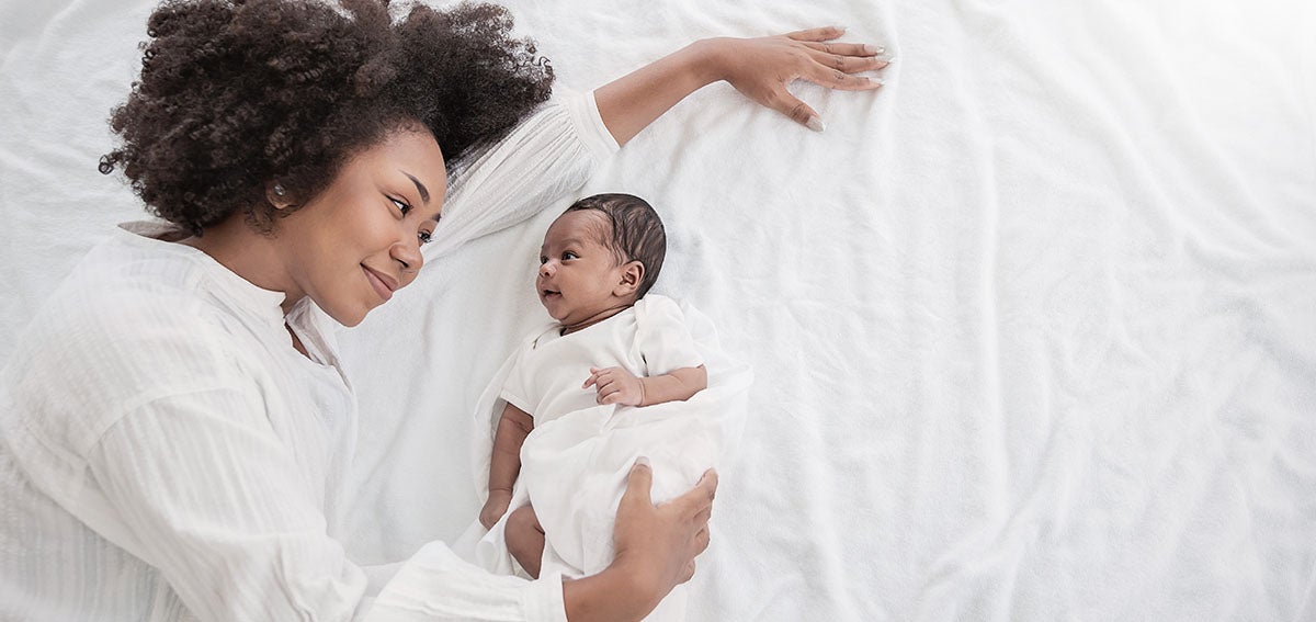 Mother lays on bed with newborn baby.