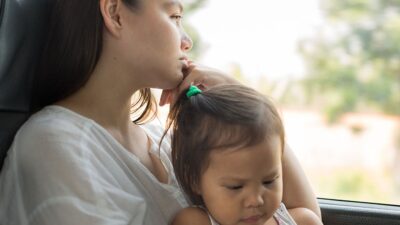 Mother holds baby and looks off into the distance, while sitting in car