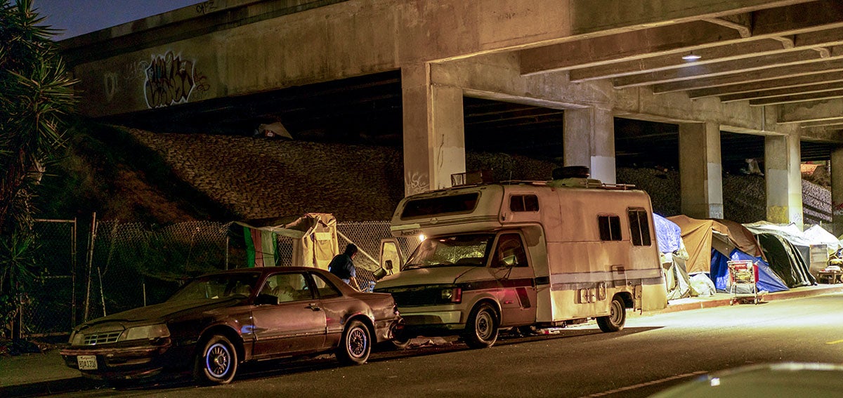 Vehicles sit parked next to tents beneath the overpass of U.S. Highway 101 in Los Angeles, California.